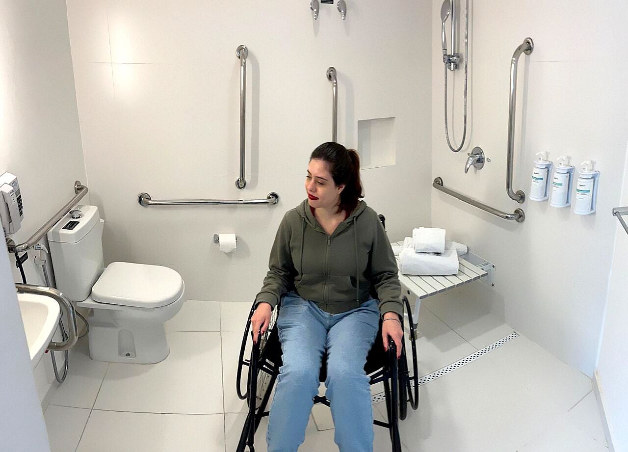 A wheelchair-accessible bathroom with a toilet, handrails, and a shower area.