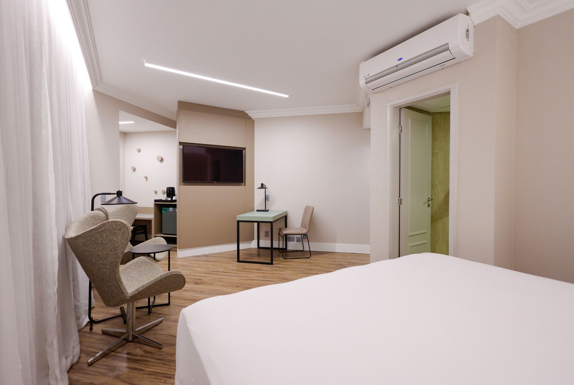 Quarto de hotel com cama, escrivaninha, cadeira, televisão e ar condicionado.