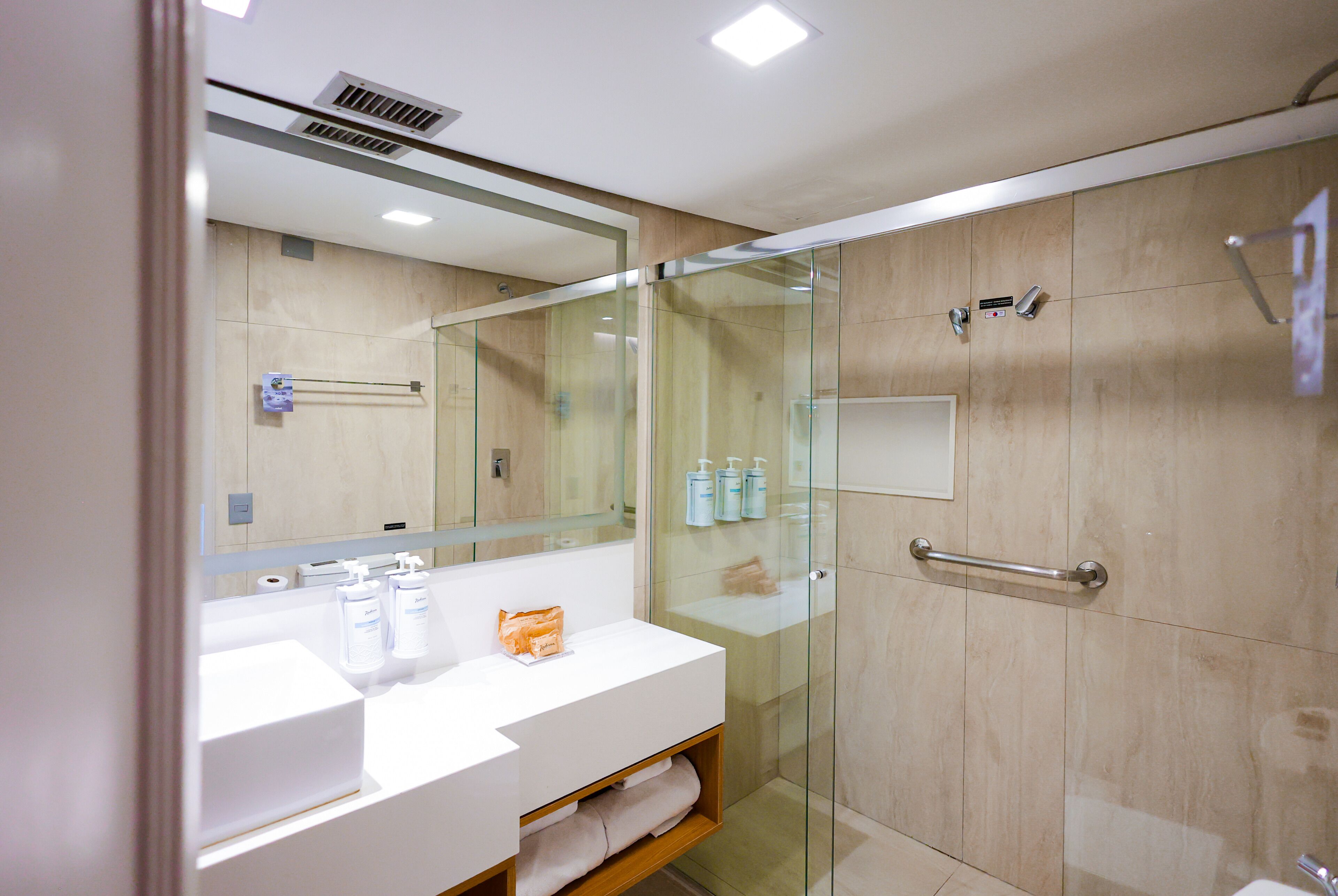 Un baño moderno con ducha de mampara de vidrio, un lavamanos blanco y un espejo sobre él.