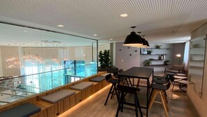 Un espacio de oficina moderno con comedor, asientos de madera y vistas a la ciudad a través de amplios ventanales.
