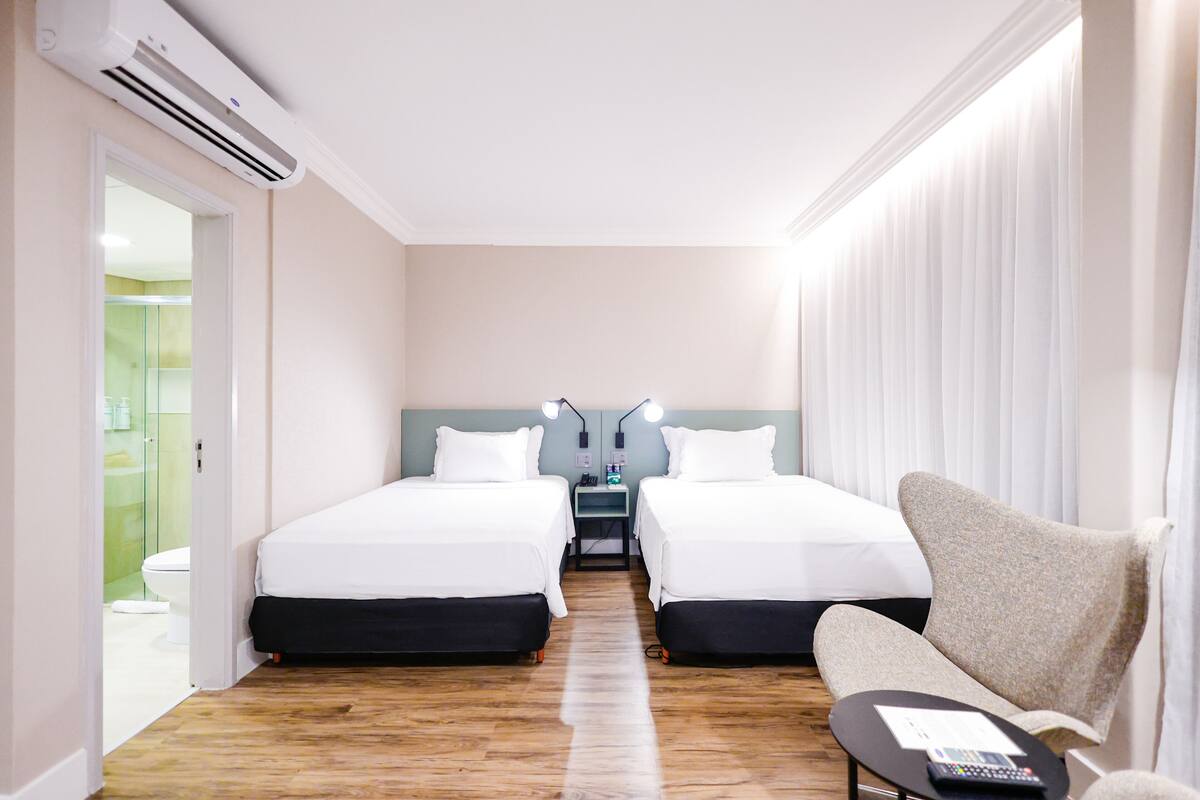 A hotel room with two beds, a desk, a chair, and an air conditioning unit.