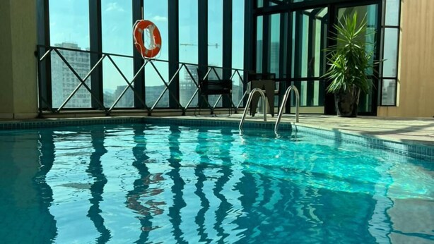 Una piscina interior con agua azul cristalina, ventanas amplias y vistas a la ciudad.