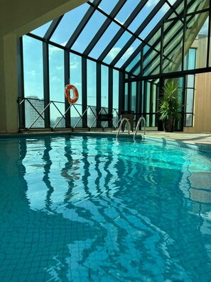 An indoor swimming pool with clear blue water, large windows, and a view of the cityscape. - Radisson Hotel Oscar Freire (São Paulo)