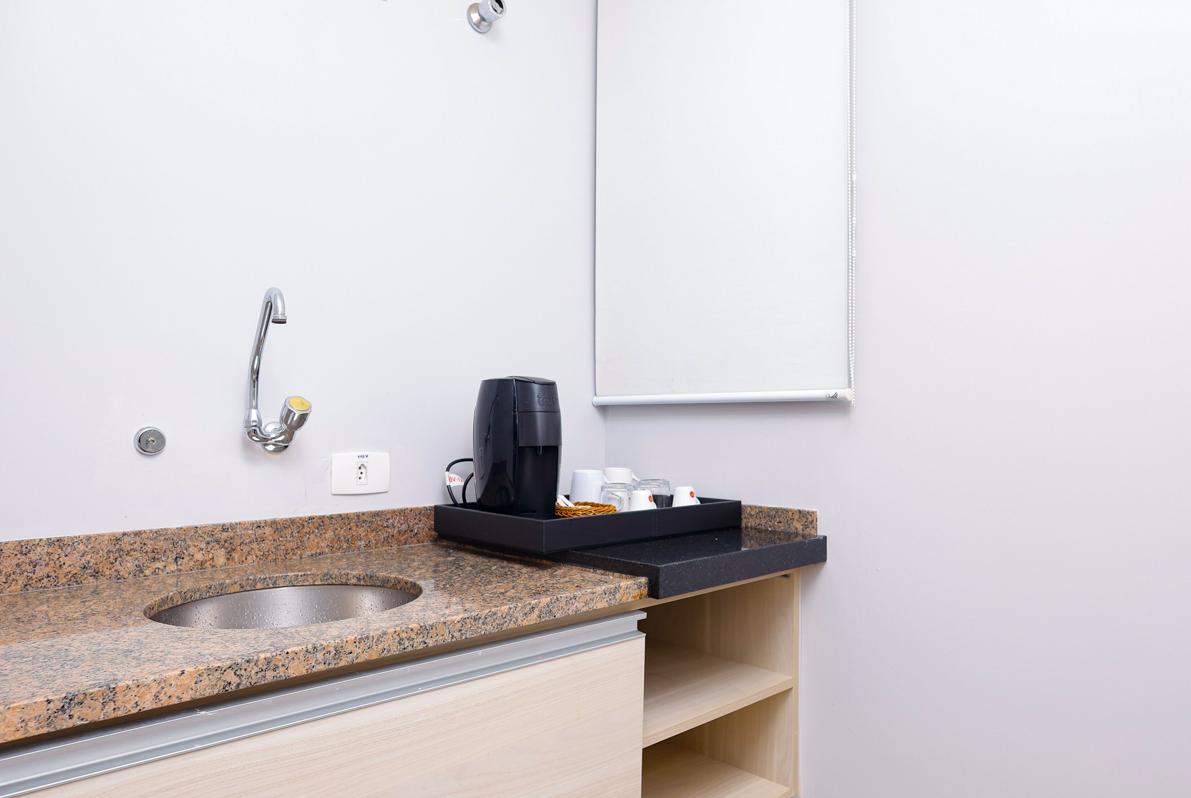 A modern bathroom with a granite countertop, a stainless steel sink, a black coffee maker, and a whiteboard on the wall.