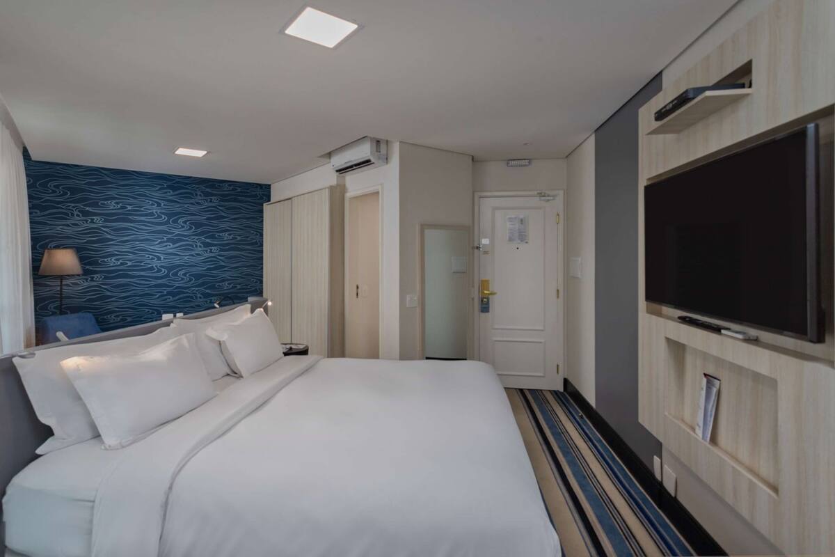 A hotel room with a bed, a TV, a desk, and a patterned wall.