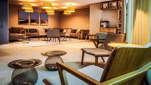 Un moderno vestíbulo de hotel con zonas de estar, iluminación colgante y una máquina de café.