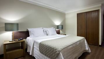 Una habitación de hotel con cama, mesitas de noche, lámparas y un armario.