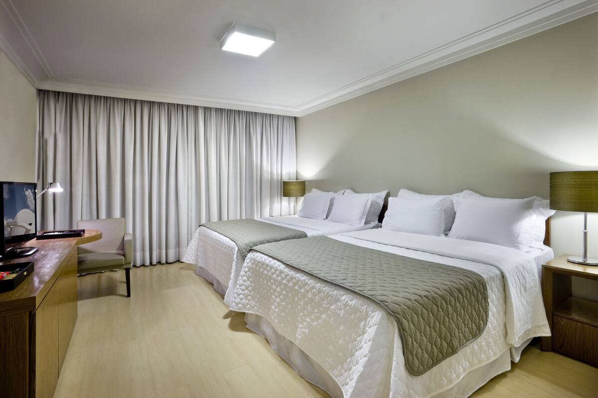 A hotel room with two beds, a desk, a chair, and a TV.