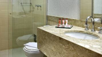 Un baño con cabina de ducha de vidrio, inodoro blanco, lavabo con encimera de mármol y espejo sobre el lavabo.