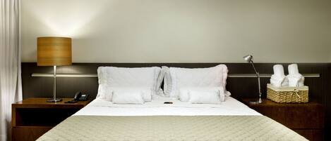 A neatly made bed with a quilted cover, a bedside lamp, a nightstand with a phone, and a basket of towels.