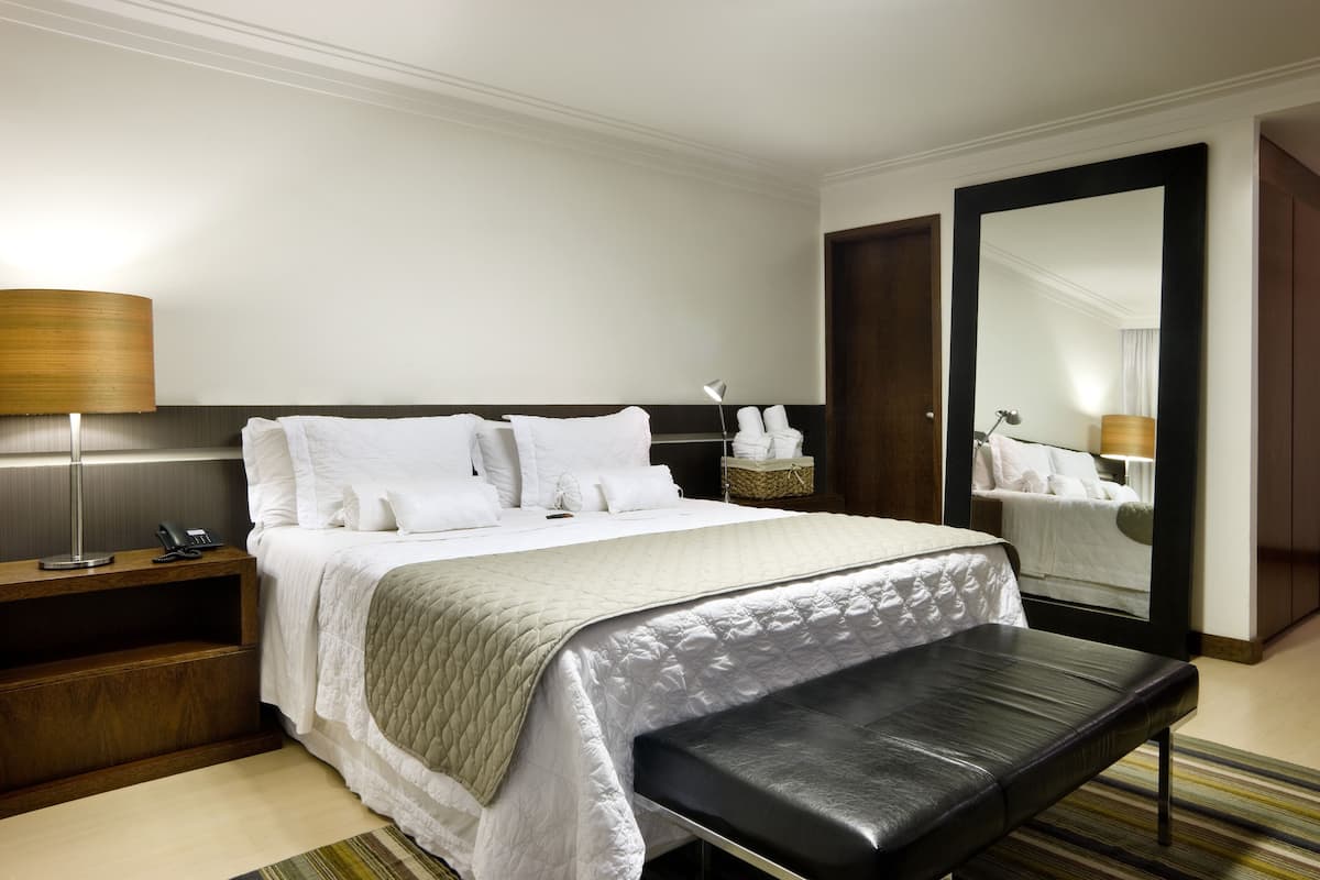 A hotel room with a bed, bedside table, lamp, and a large mirror.