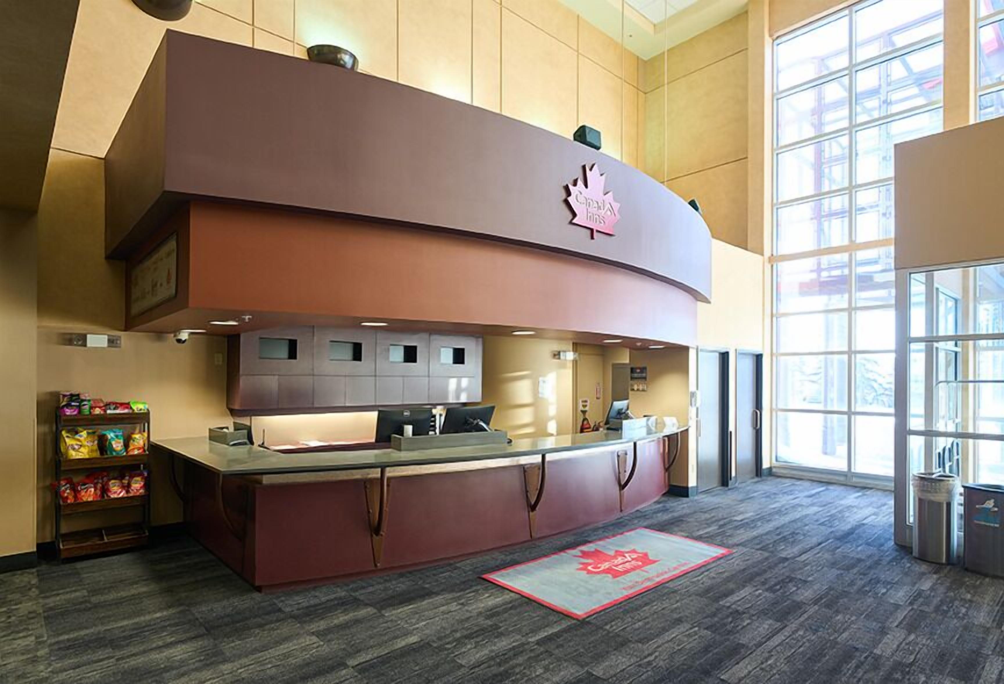 A hotel reception area with a large counter, a Canadian flag logo, and a window providing natural light.
