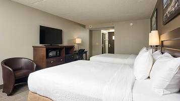 Una habitación de hotel con cama, escritorio, silla, televisor y lámpara.