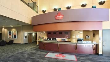 Mostrador de recepción de Canada Inn, con un mostrador de registro, una escalera de cristal y suelo alfombrado.