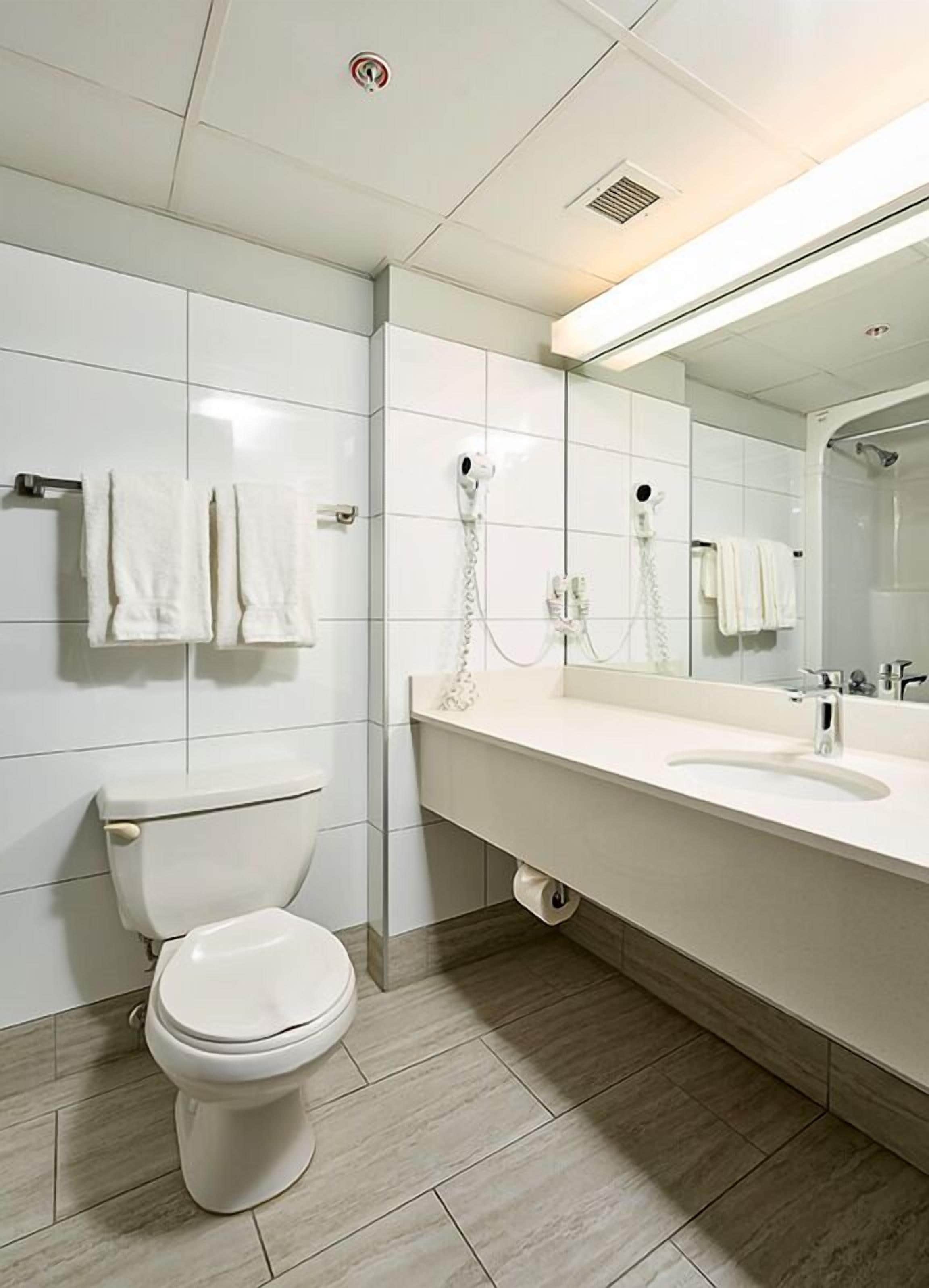 A modern bathroom with a toilet, a sink, a mirror, and a hairdryer mounted on the wall.