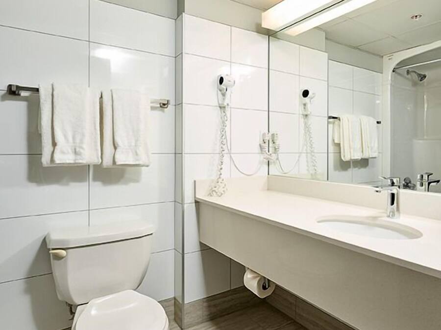 A modern bathroom with a toilet, a sink, a mirror, and a hairdryer mounted on the wall.