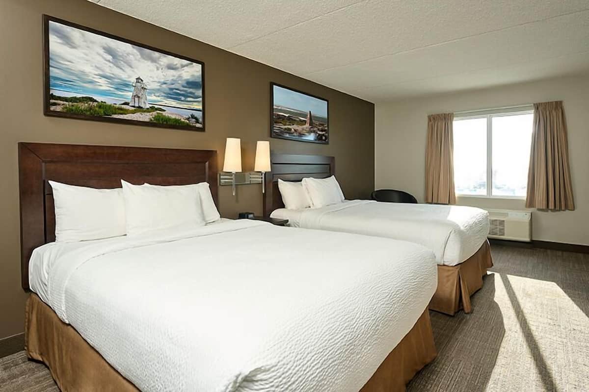 Quarto de hotel com duas camas, uma escrivaninha, uma cadeira, janela com cortinas e duas luminárias fixadas na parede.