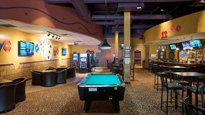 Una mesa de billar en una sala con juegos de arcade, una zona de bar y asientos.