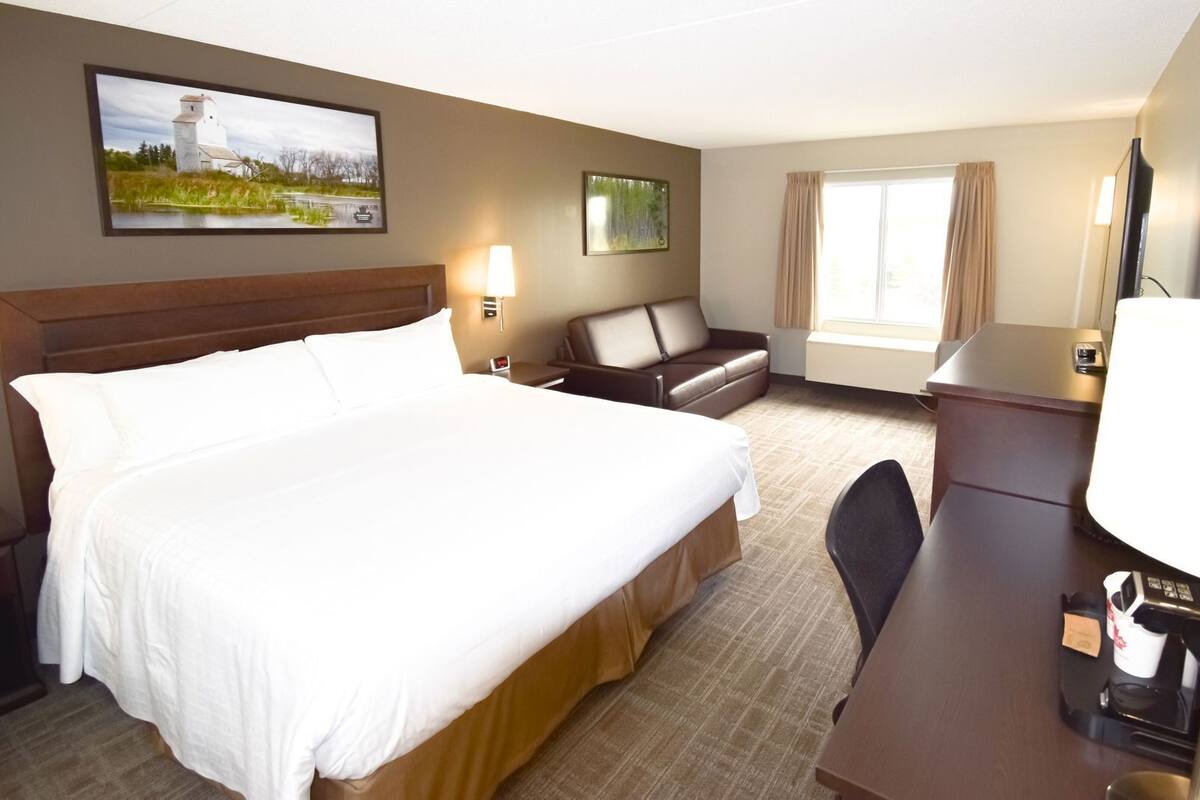 Quarto de hotel com cama grande, escrivaninha, cadeira, sofá, televisão e obras de arte nas paredes.