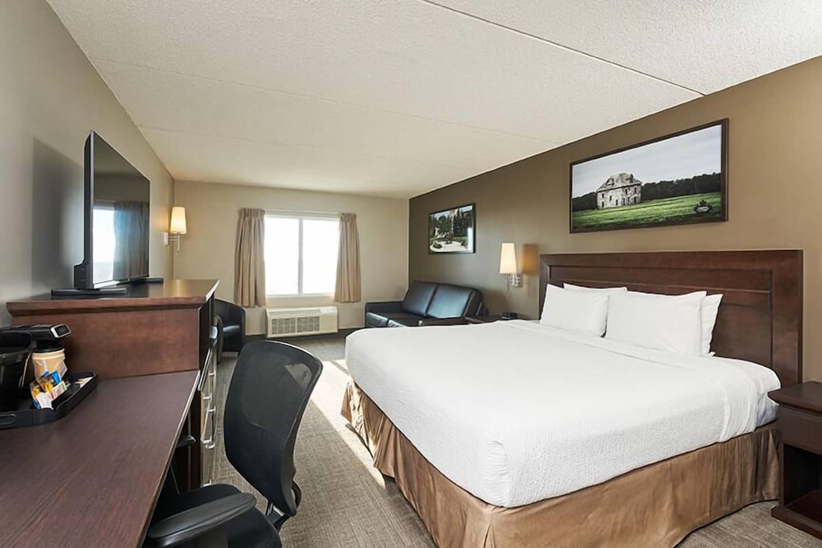 Quarto de hotel com cama, escrivaninha, cadeira, televisão e duas pinturas na parede.