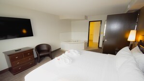 Habitación de hotel con cama, televisión, escritorio, silla, bañera y puerta.