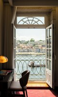 A room with a view of a river, a chair, a desk with a lamp, and a window with a metal railing.