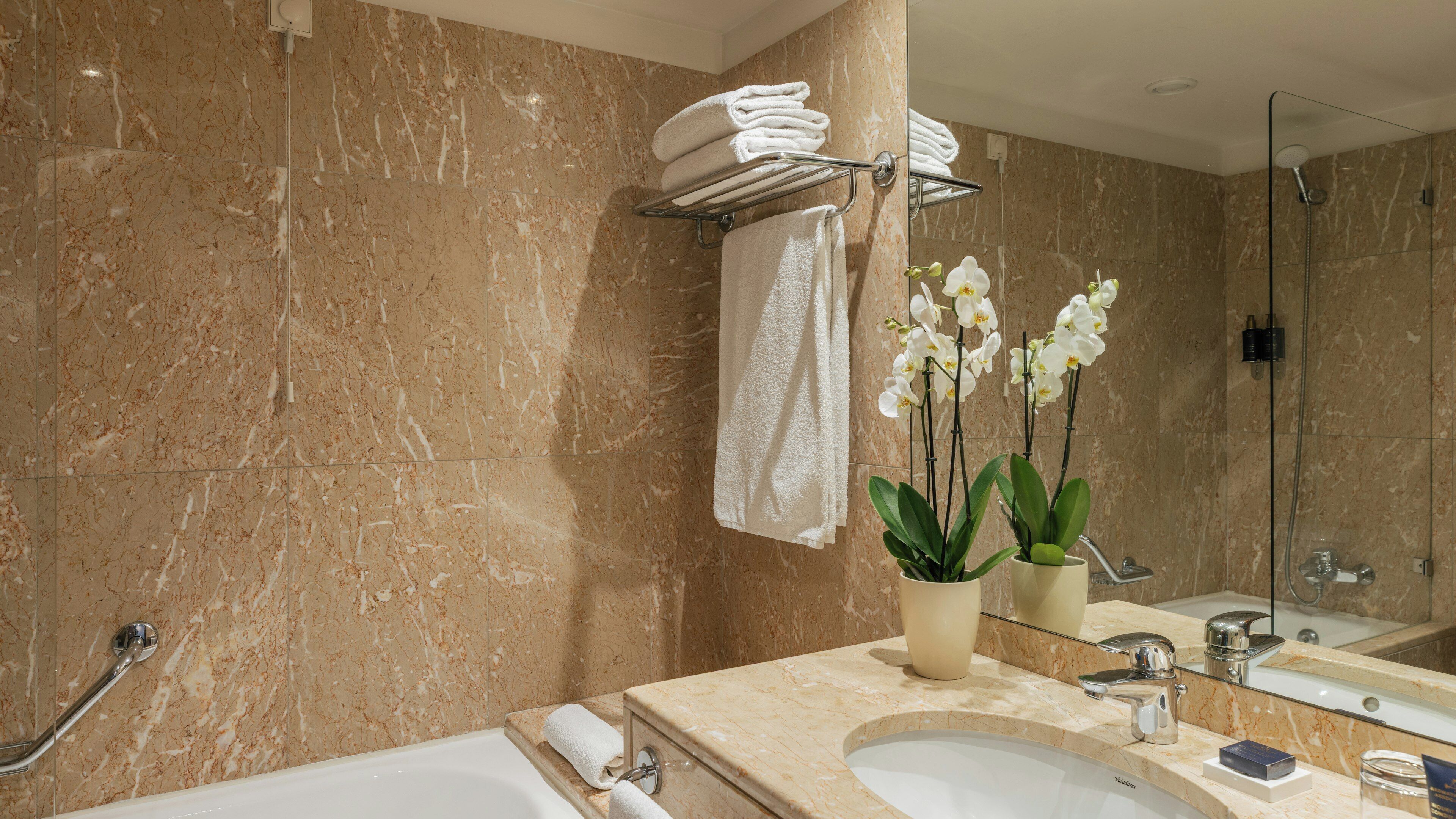 Un baño con pared de mármol, una bañera, un lavabo, un espejo y una ducha.