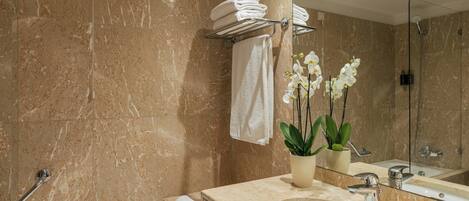 A bathroom with a marble wall, a bathtub, a sink, a mirror, and a shower.