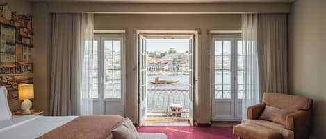 Une chambre d’hôtel avec un lit, une chaise, une vue sur le paysage urbain depuis un balcon et un tableau accroché au mur.