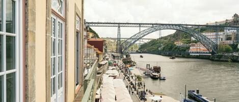 A riverside walkway with a bridge in the background, a boat docked on the river, and buildings along the riverbank.