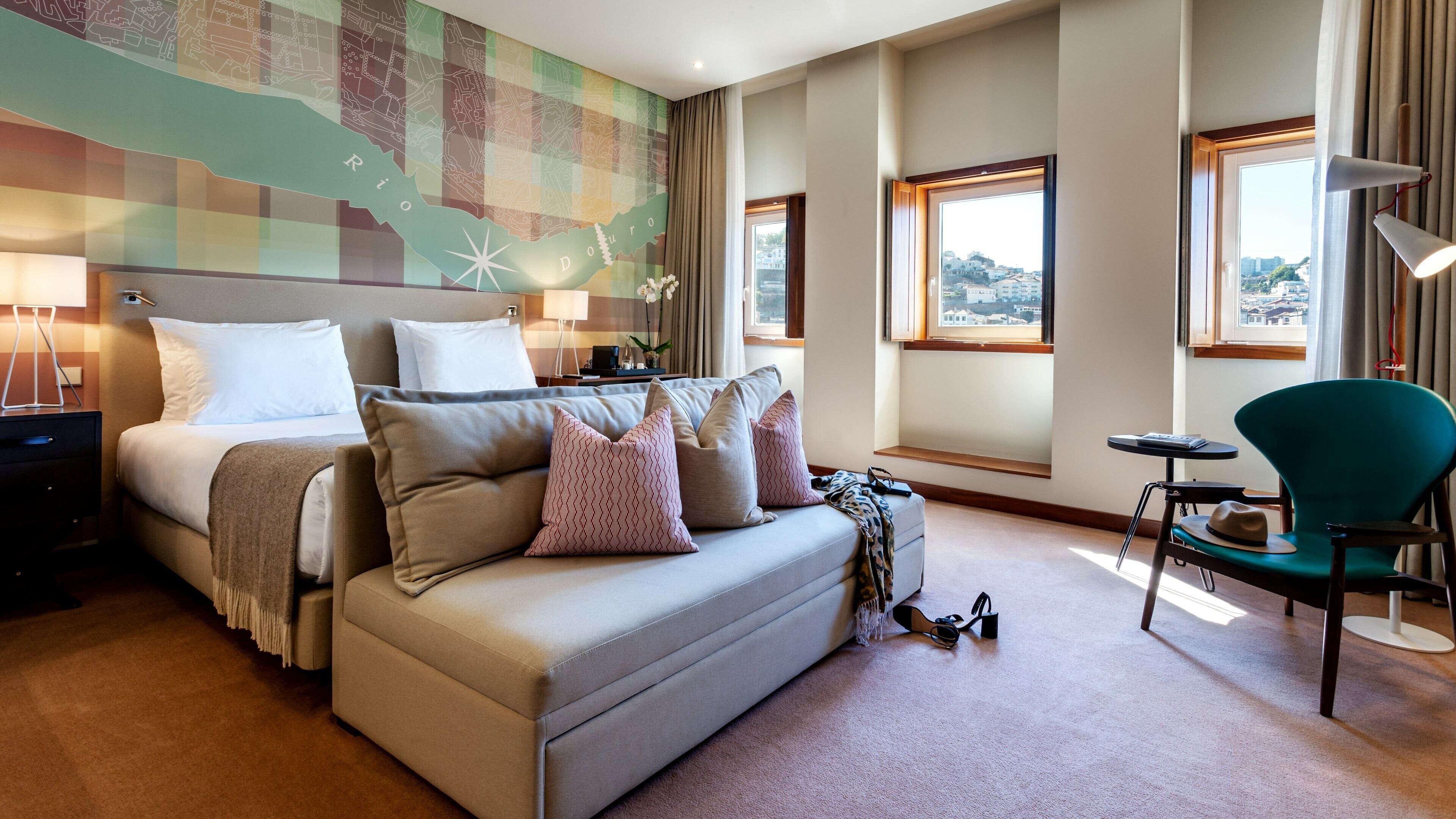 A hotel room with a bed, a sofa, a window with a view, a lamp, and a chair.