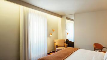 Una habitación de hotel con cama, una silla, un escritorio y un espejo grande.