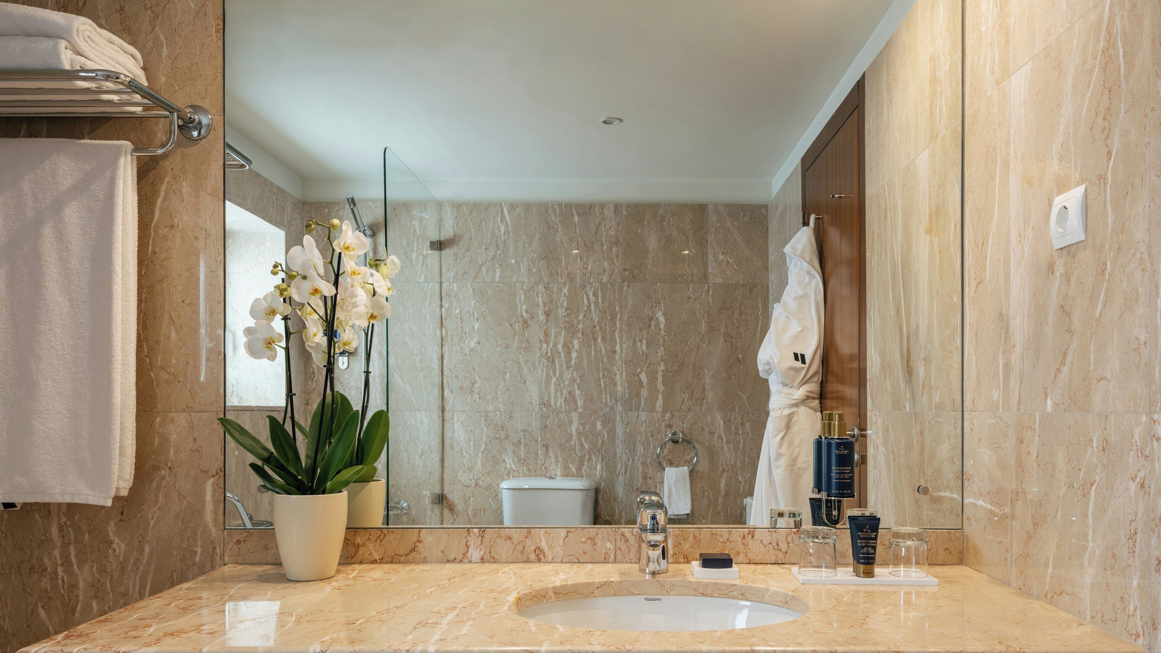 Un bagno con un lavandino in marmo, un'orchidea in vaso, un portasciugamani e uno specchio.