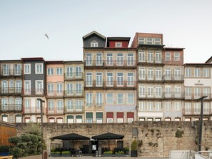 A row of multi-story buildings with balconies, a stone wall in the foreground, and outdoor seating with umbrellas. - Pestana Vintage Porto Hotel & World Heritage Site (Porto)