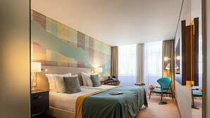 Hotellihuone, jossa on suuri sänky, työpöytä, tuoli ja seinällä kartta.