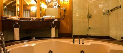 A bathroom with a large bathtub, a mirror, and a glass shower enclosure.