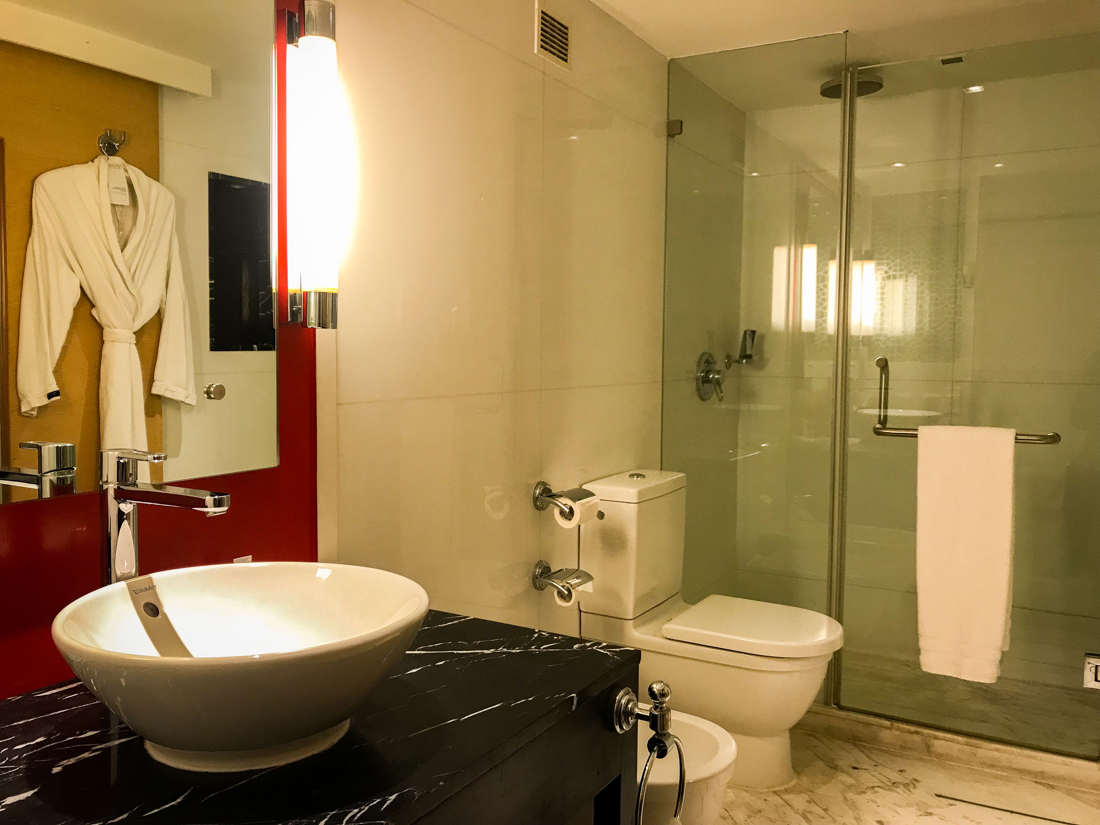 Une salle de bain moderne avec une douche à parois de verre, des toilettes blanches et un grand lavabo sur colonne.