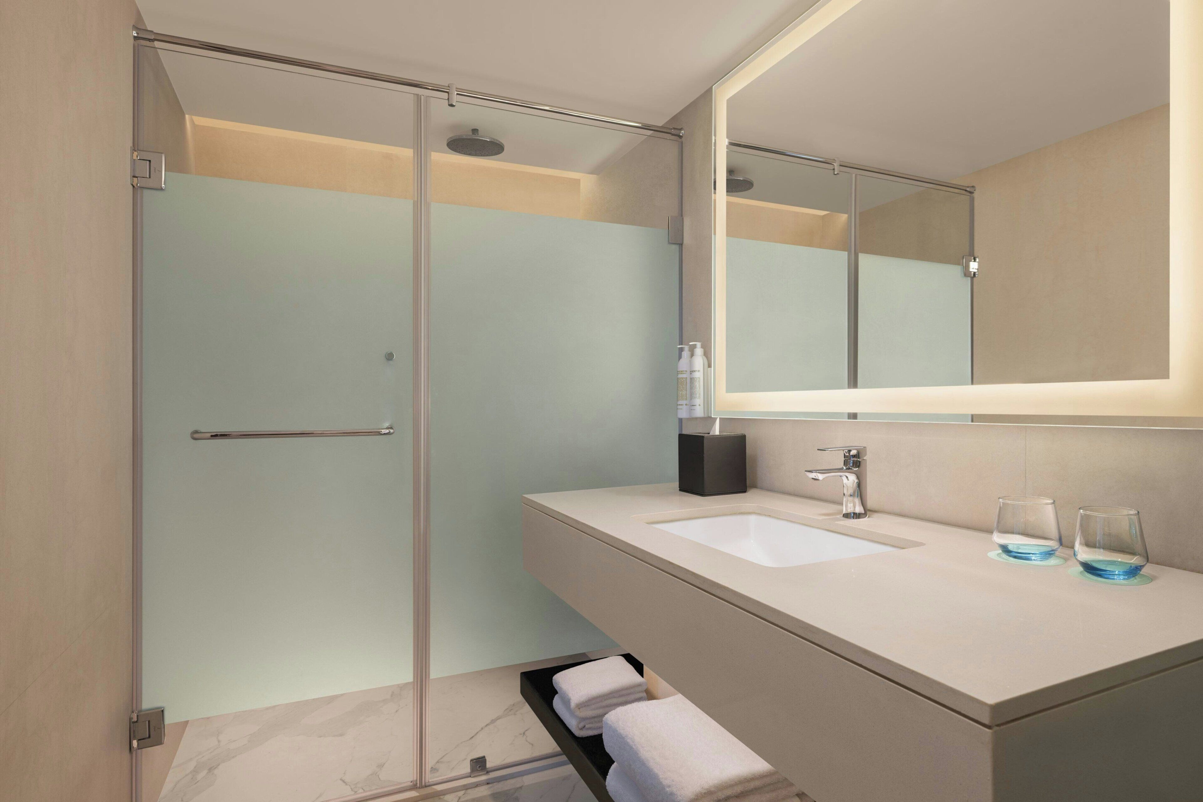 Een moderne badkamer met een douchecabine van glas, een wastafel met spiegel en twee glazen op het aanrecht.