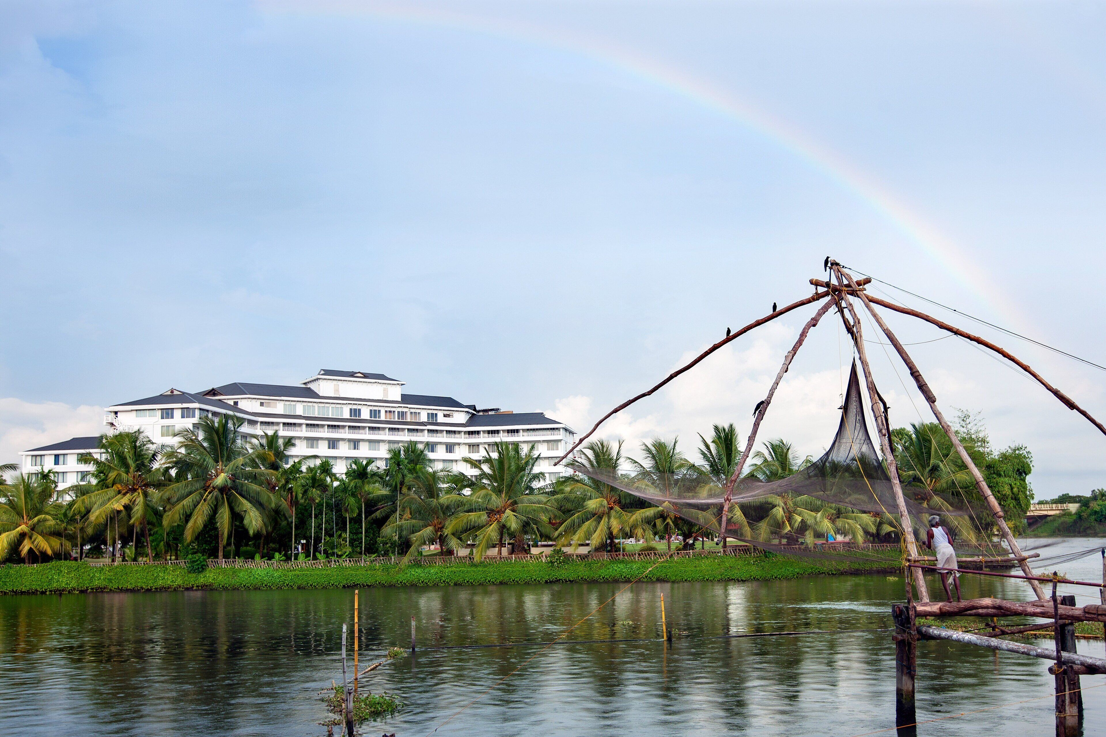 A hotel with a large building, palm trees, and a fishing net structure over water.
