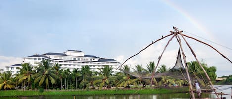 A hotel with a large building, palm trees, and a fishing net structure over water.