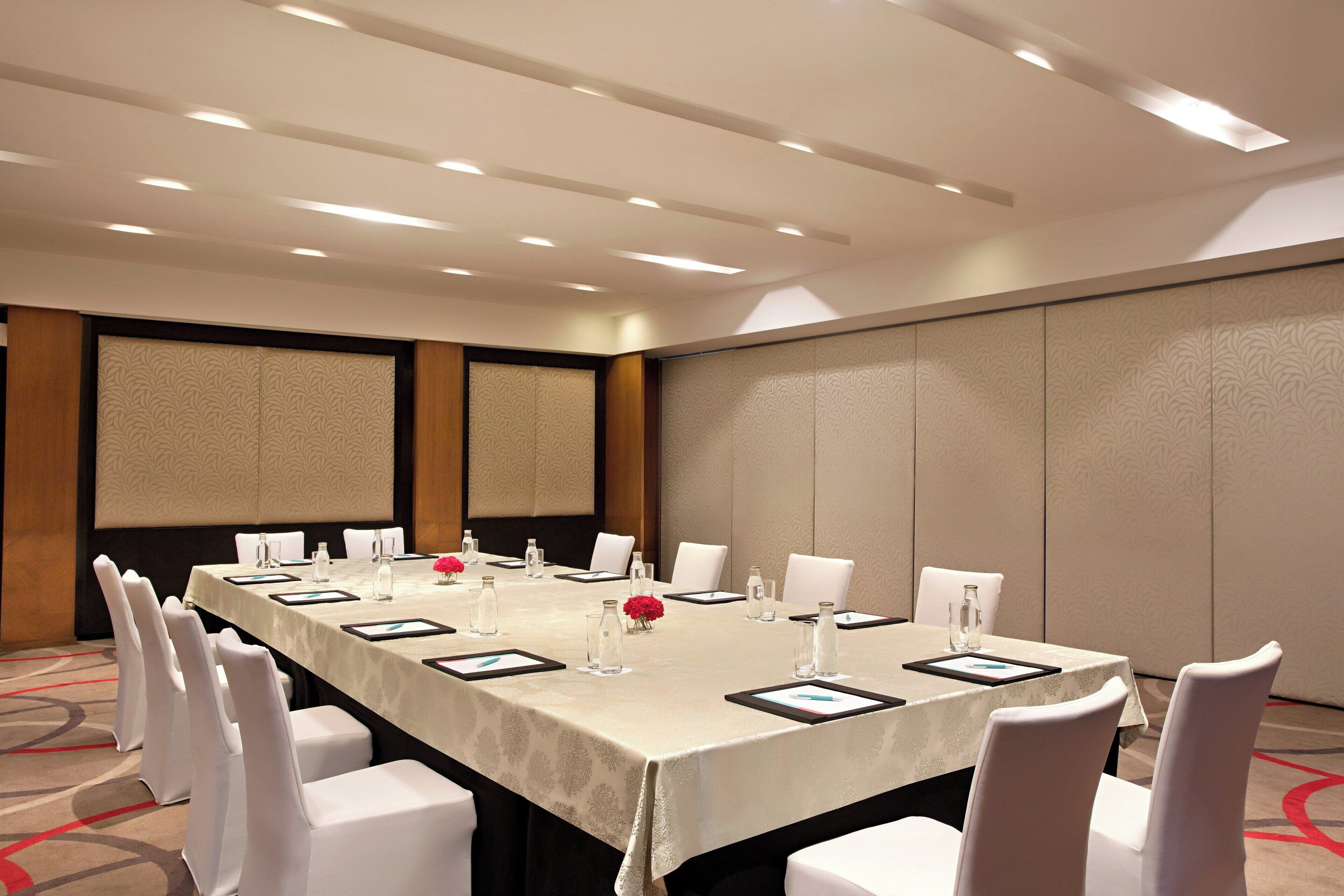 A conference room with a long table, white chairs, and a beige tablecloth.