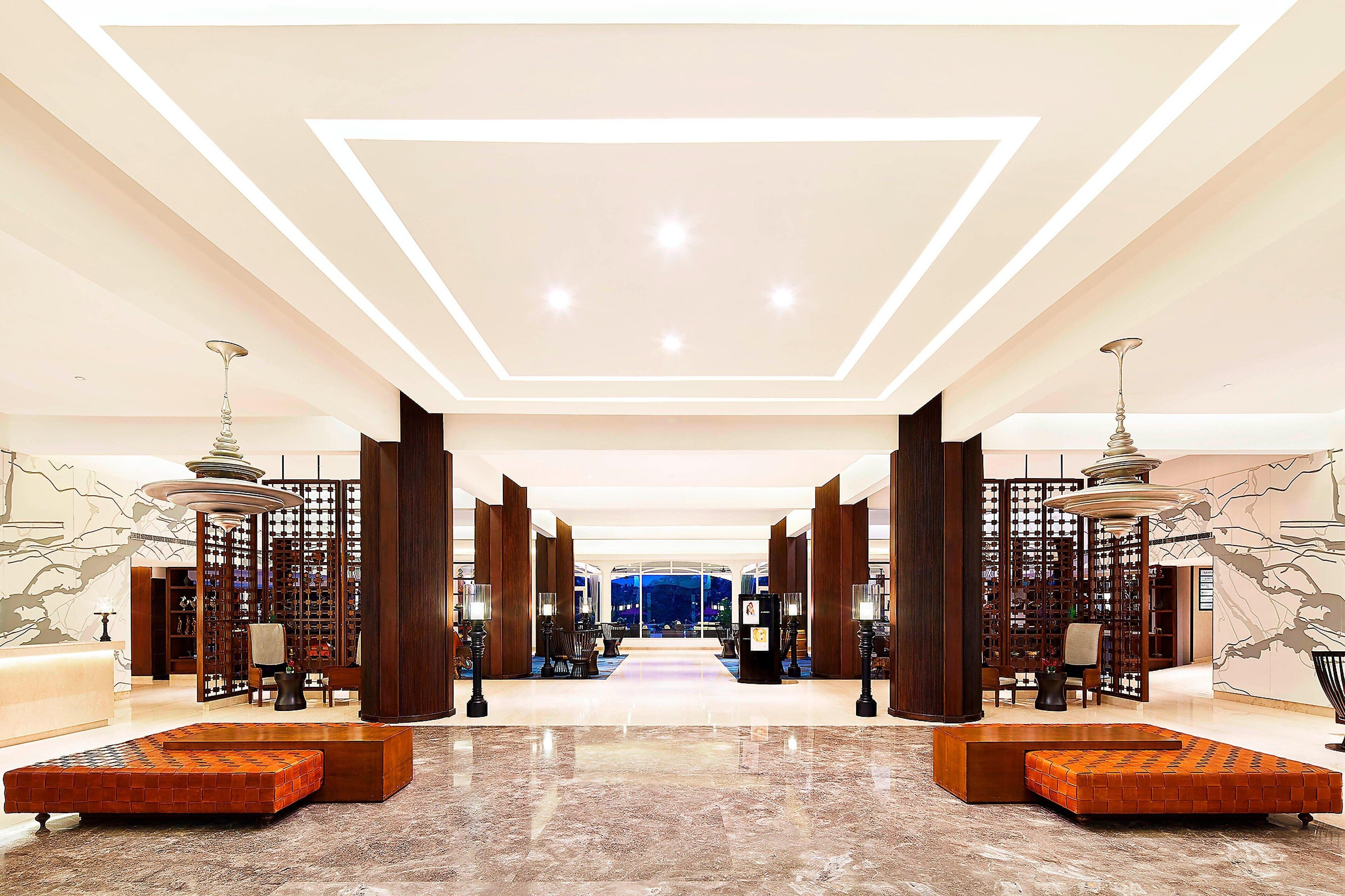Eine geräumige Lobby mit einer zentralen Sitzecke, einer hohen Decke mit eingelassener Beleuchtung und Blick durch die Glaswand nach draußen.