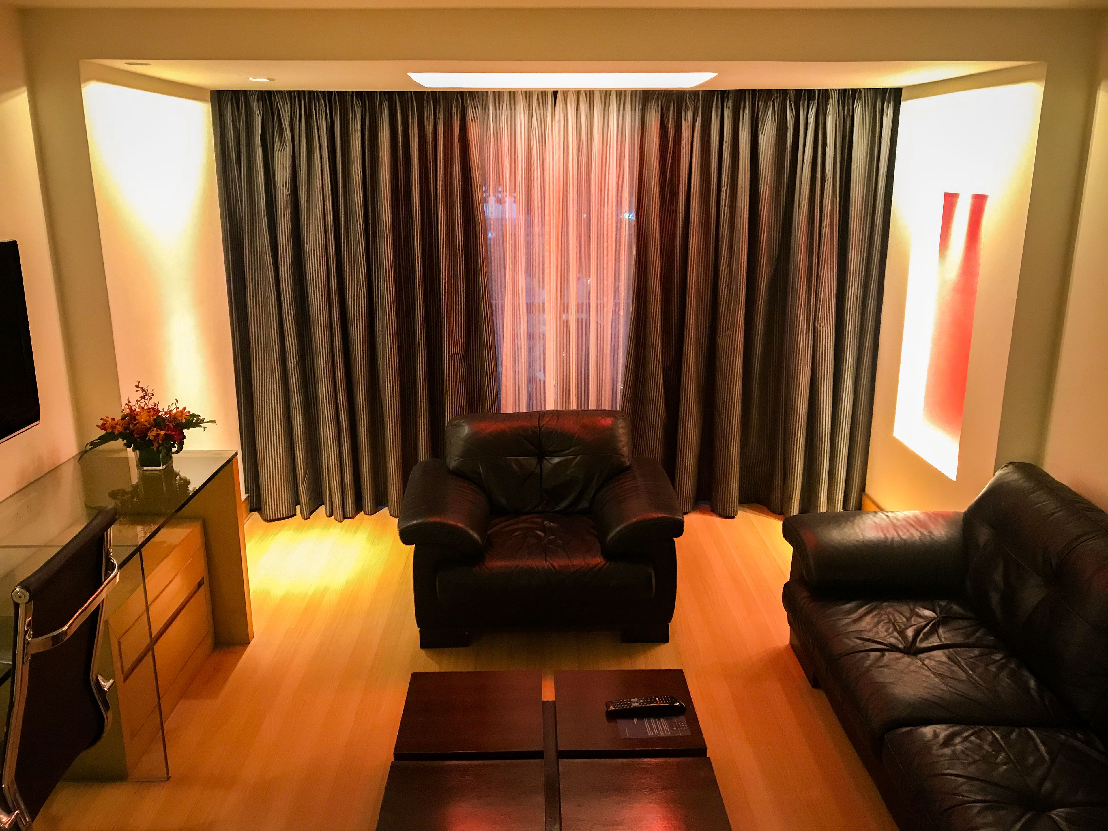 A living room with a leather sofa, a glass coffee table, and a TV on the wall.