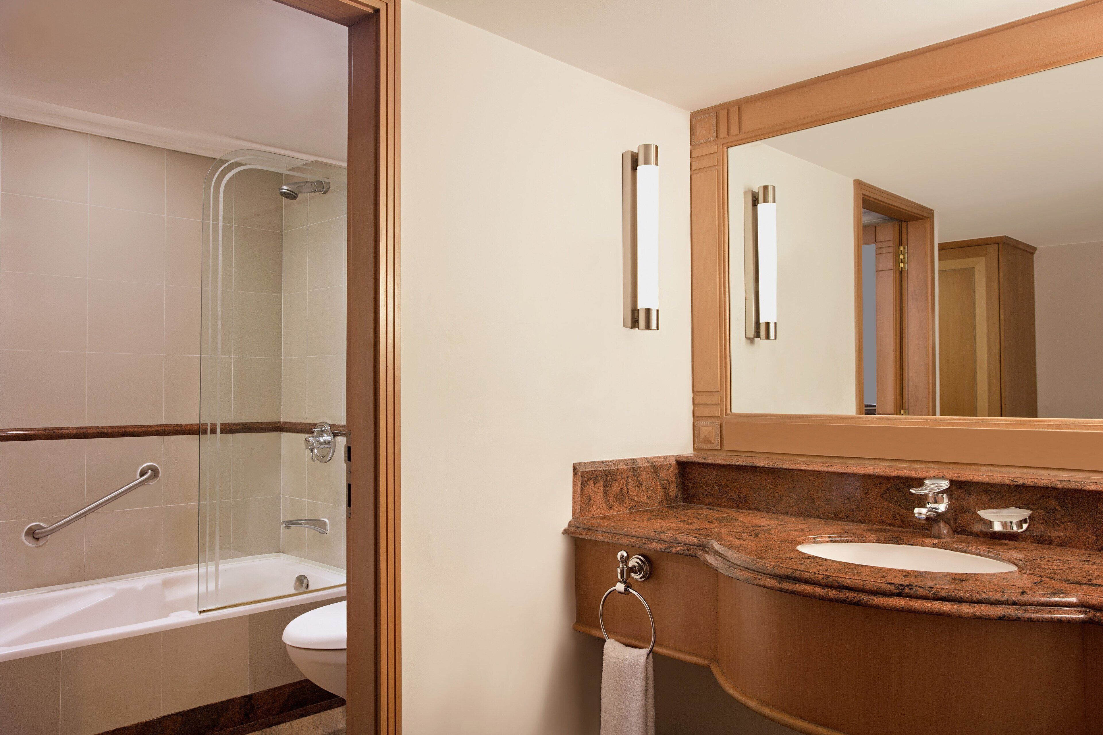 A bathroom with a glass shower enclosure, a sink with a marble countertop, and a large mirror above the sink.