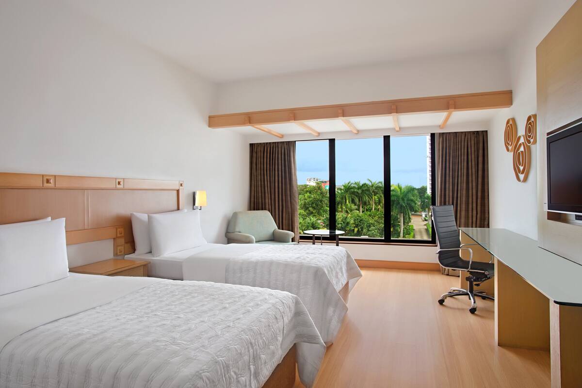 A hotel room with two beds, a desk, a chair, and a TV.