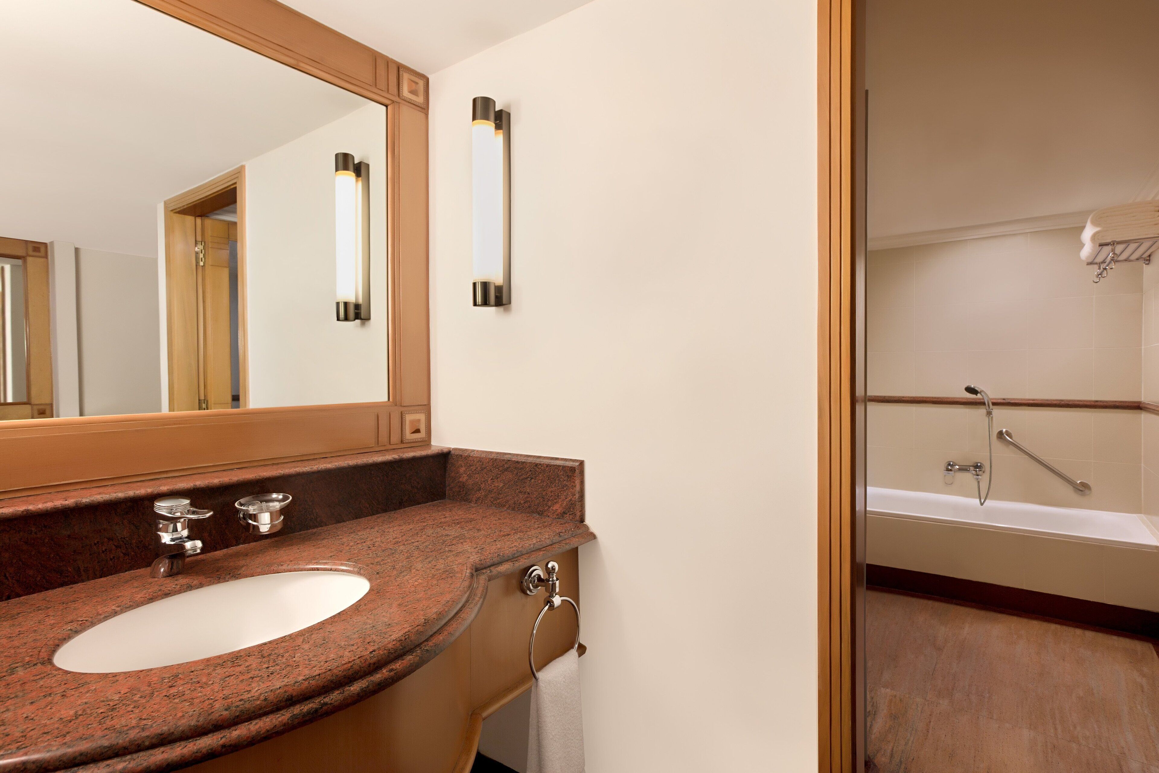A bathroom with a granite countertop sink, a mirror, a towel rack, and a shower area.