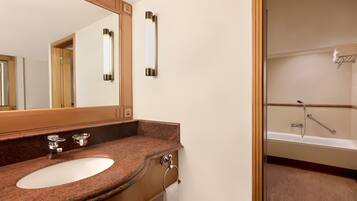 A bathroom with a granite countertop sink, a mirror, a towel rack, and a shower area.