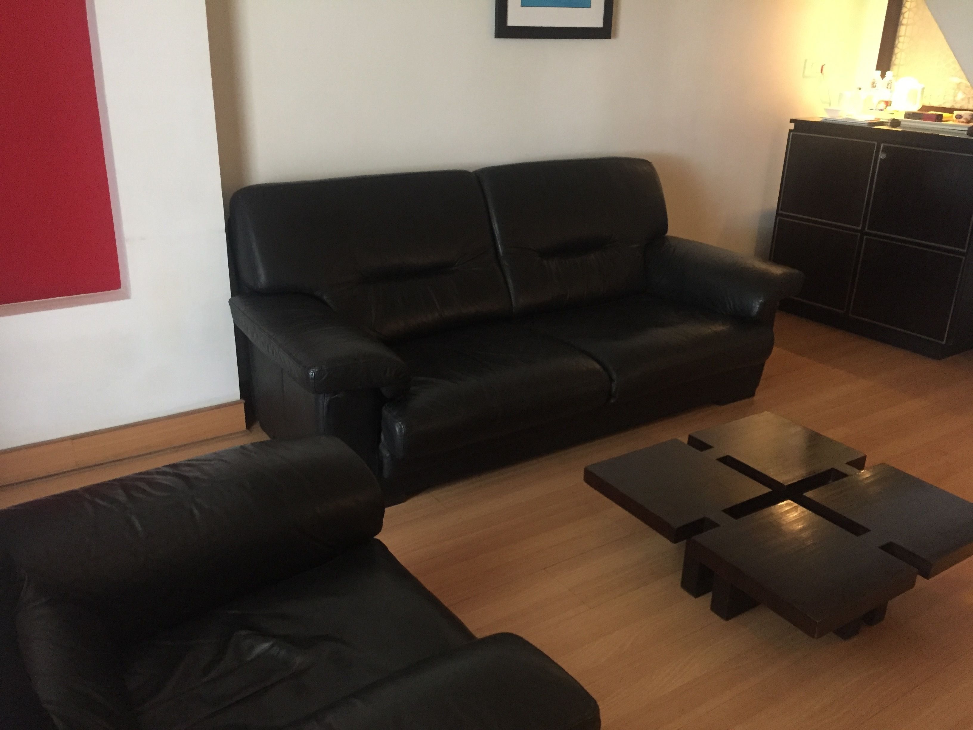 A living room with a black leather sofa, a wooden coffee table, and a cabinet.