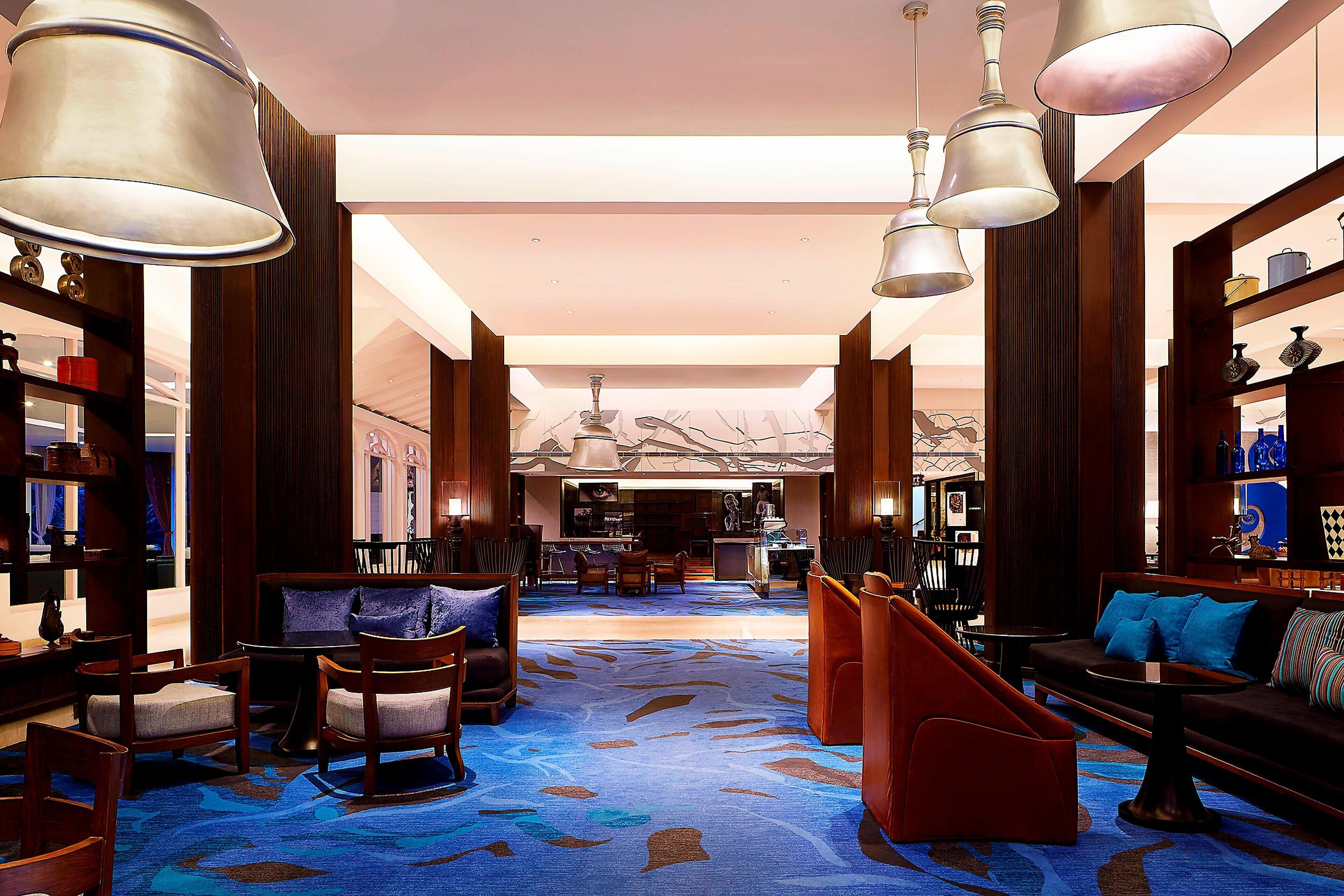 Eine geräumige Lobby mit blauem Teppich, Holzmöbeln und hängenden Lampen.