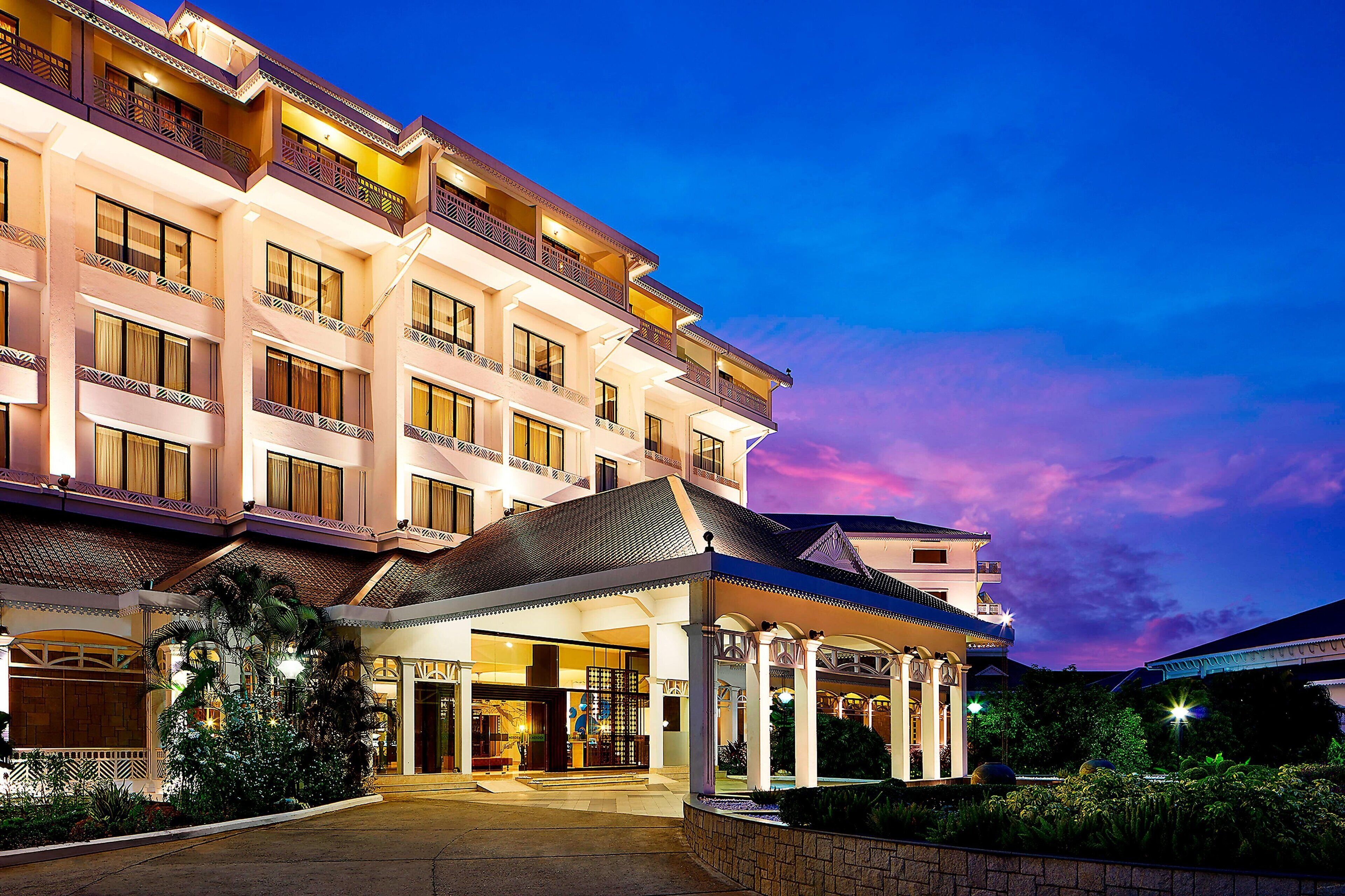 A multi-story hotel with a traditional architectural style, featuring balconies and a well-lit entrance.